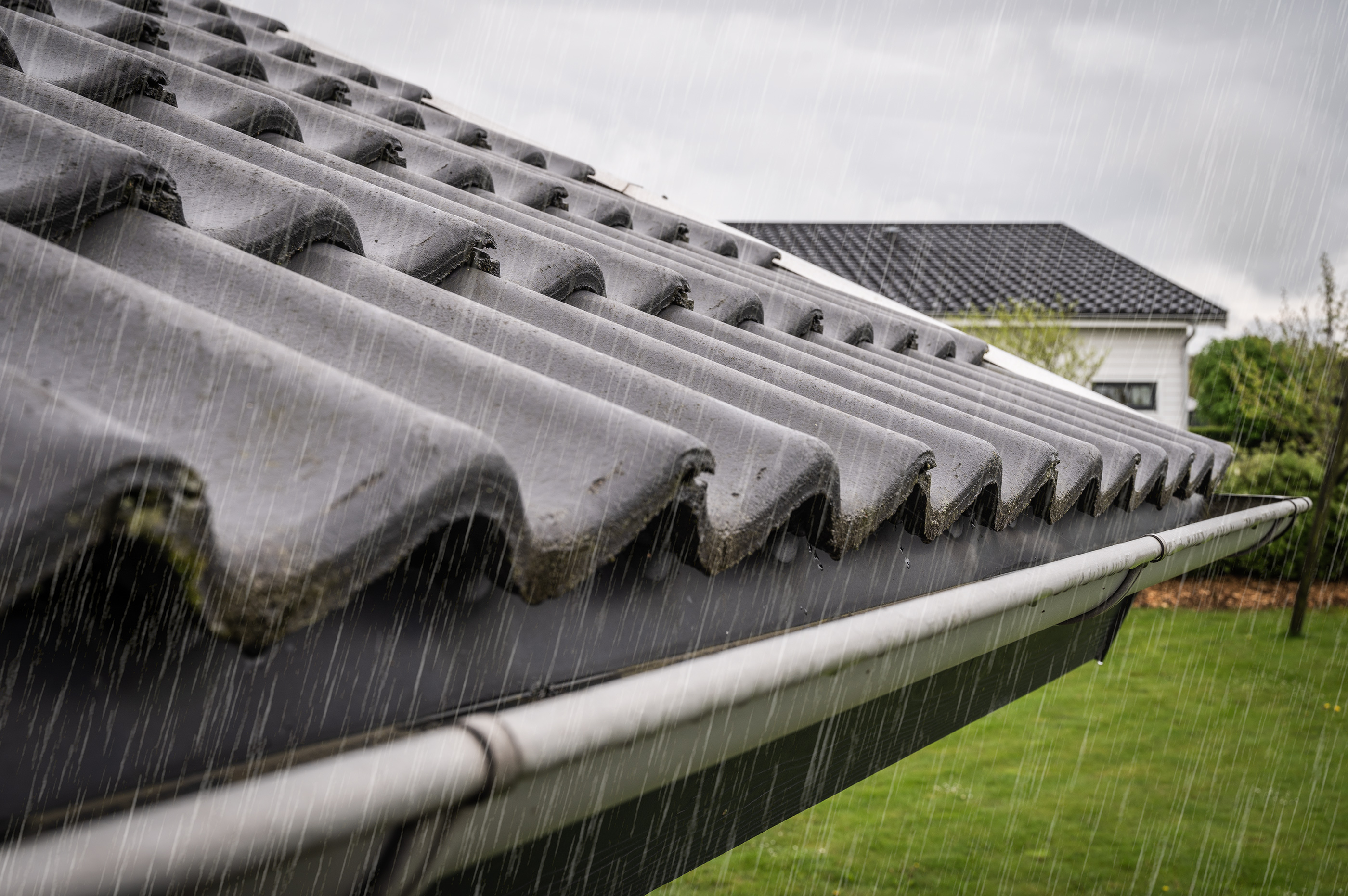 Regndråber løber ned ad rør eller taglate under en grå, overskyet himmel.